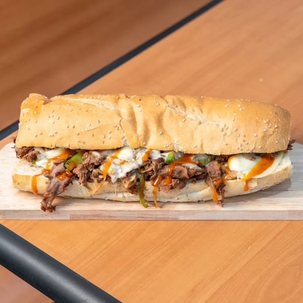 Capones Italian Eatery West's cheesesteak sandwich with steak, cheese, peppers, and sauce on a wooden board.