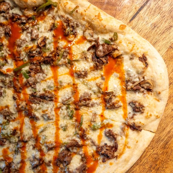 Close-up of a Capones Italian Eatery West pizza with cheese, meat, green peppers, and hot sauce.