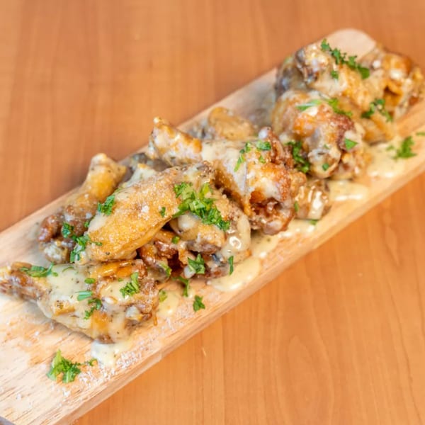 Garlic Parmesan chicken wings on a wooden board, drizzled with sauce and garnished with parsley.