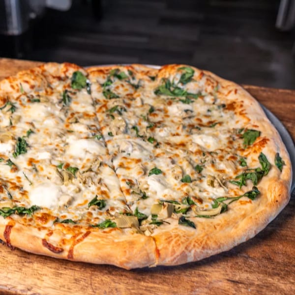 A white pizza with spinach and artichoke hearts, sliced and ready to eat.