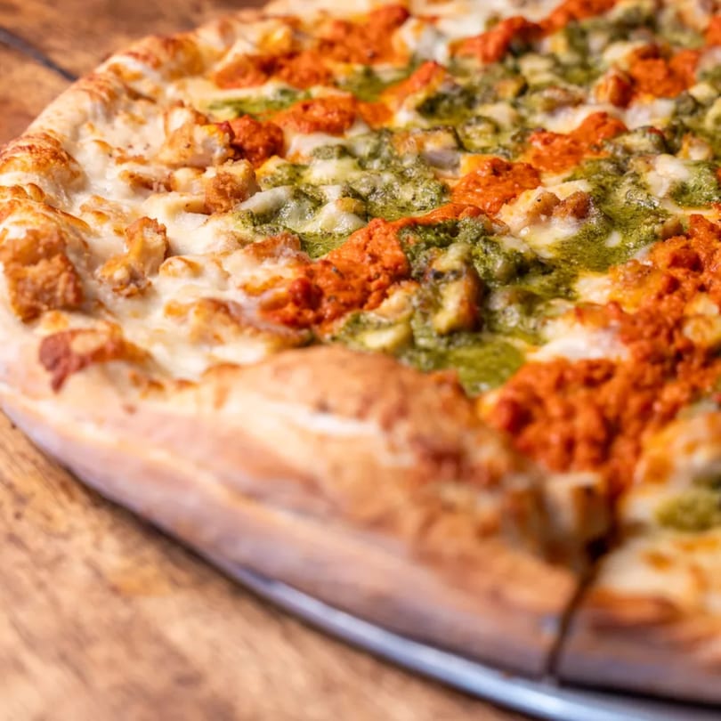 Close-up of a Capones Italian Eatery West pizza with pesto, red sauce, and chicken.